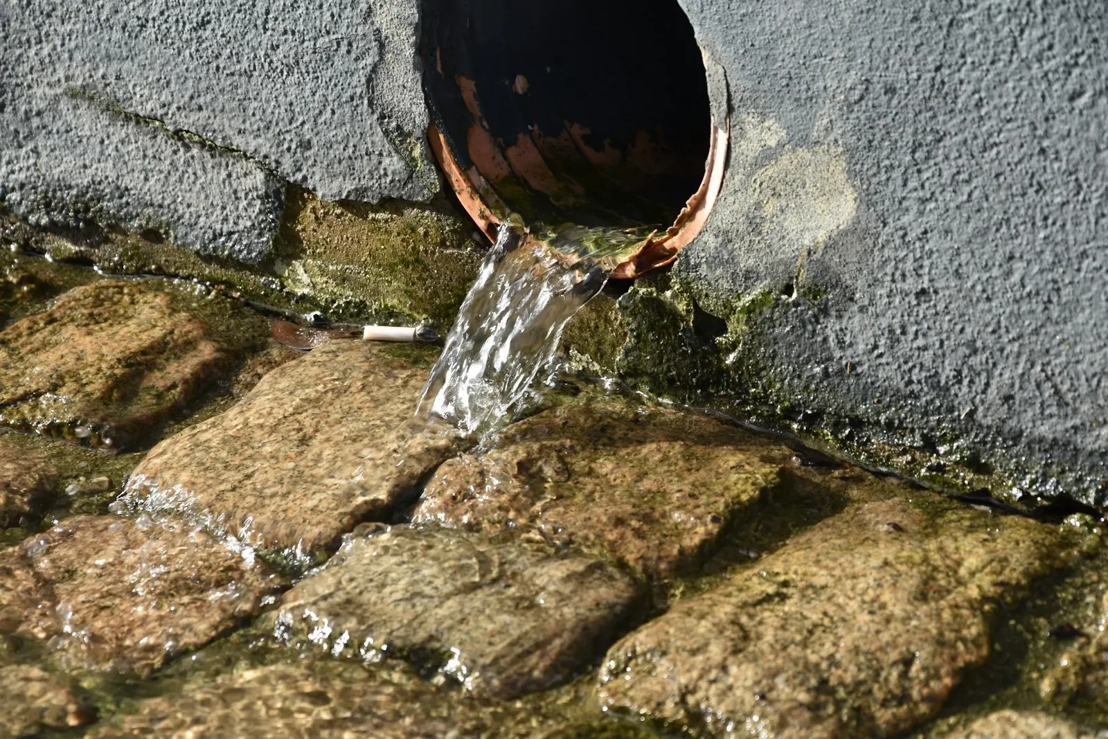 Rainwater downpipe beside a cobbled surface